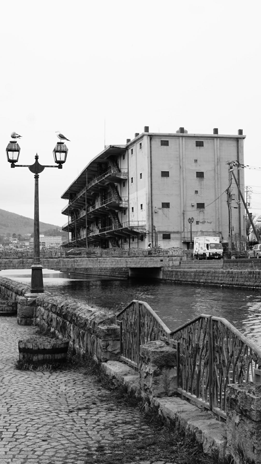 A canal-side warehouse building with seagulls on a lamppost