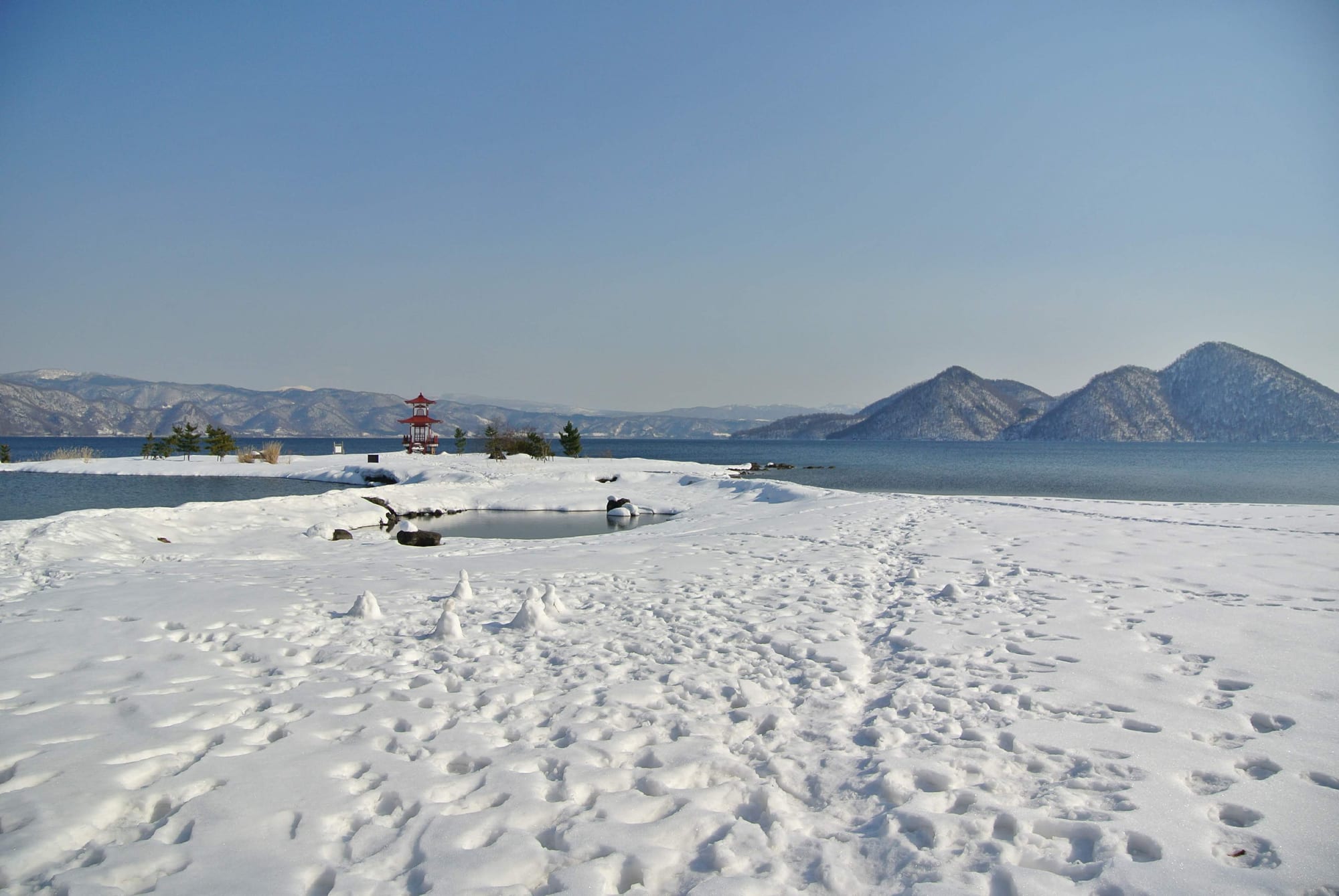 A lake with a red pagoda and footprints in the snow