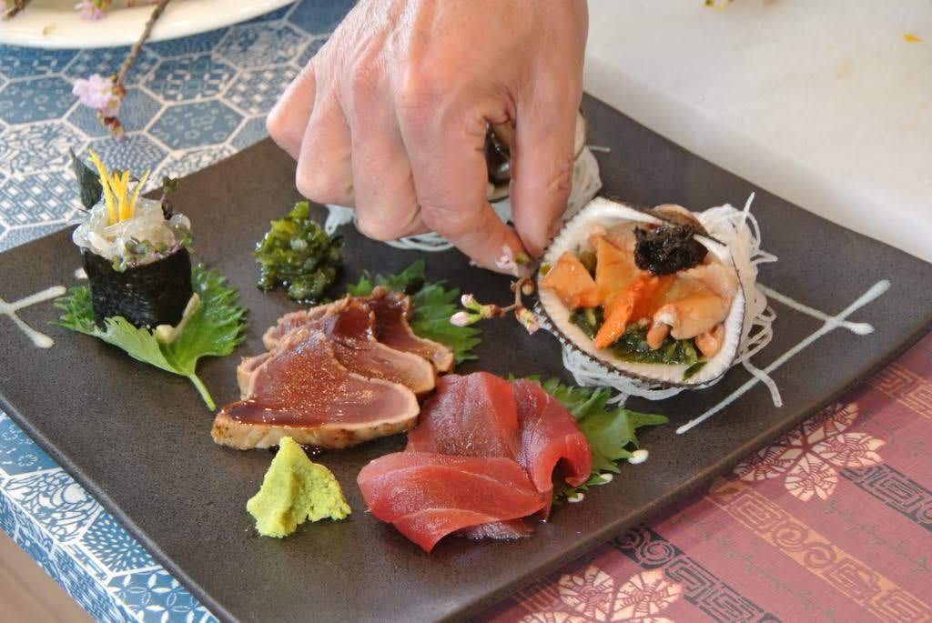 A hand arranging a plate of sashimi and abalone
