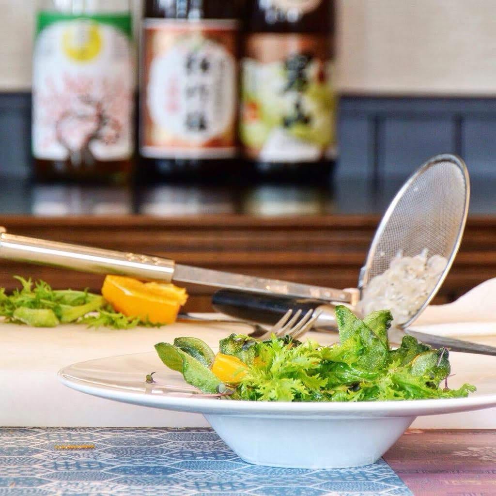 A fresh salad plated with sake bottles in the background